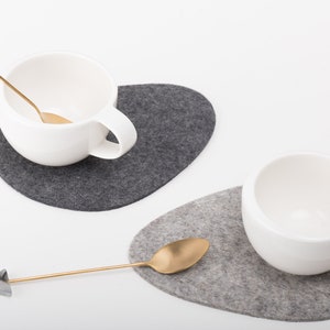 May include: Two white ceramic mugs with gold spoons on gray felt coasters. The coasters are shaped like pebbles.