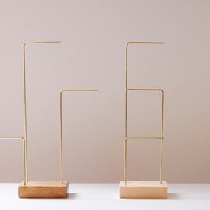 May include: Two gold metal jewelry stands with wooden bases. The stand on the left has one horizontal bar, while the stand on the right has three horizontal bars.