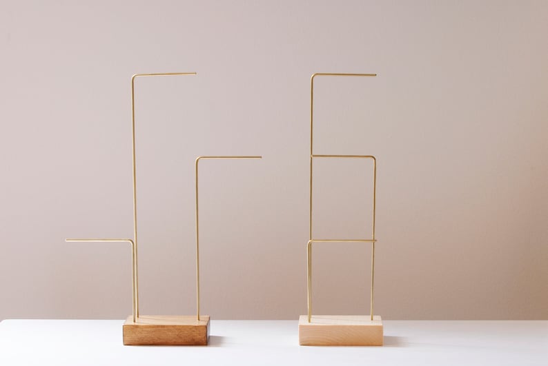 May include: Two gold metal jewelry stands with wooden bases. The stand on the left has one horizontal bar, while the stand on the right has three horizontal bars.