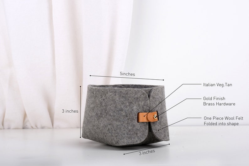 May include: A gray felt storage basket with a tan leather strap and brass hardware. The basket measures 5 inches wide and 3 inches tall.