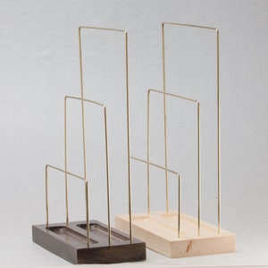 May include: Two jewellery display stands. One has a dark brown wooden base, the other a light wood base. Both have gold-coloured metal wire frames in a tiered design. The stands are designed to hold necklaces, bracelets, or other jewellery items.