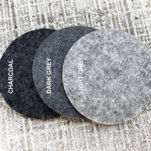 May include: Three round felt coasters in charcoal, dark grey, and light grey. The coasters are arranged in a row from darkest to lightest.