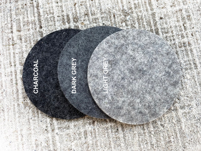 May include: Three round felt coasters in charcoal, dark grey, and light grey. The coasters are arranged in a row from darkest to lightest.