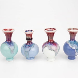May include: Four small ceramic vases with a round body and a narrow neck. The vases are decorated with a blue, white, and purple glaze. The glaze has a mottled effect, giving the vases a unique look.