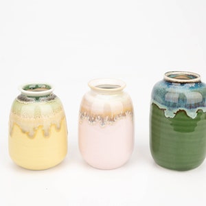 Puede incluir: Tres jarrones de cerámica con un acabado de esmalte de goteo. Los jarrones son amarillos, rosados y verdes.