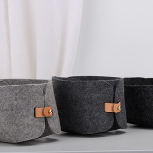 May include: Three felt storage baskets with leather handles. The baskets are gray, dark gray, and black.