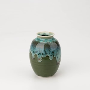 May include: A small, green ceramic vase with a blue and green glaze. The glaze has a drip effect, creating a unique and artistic look.