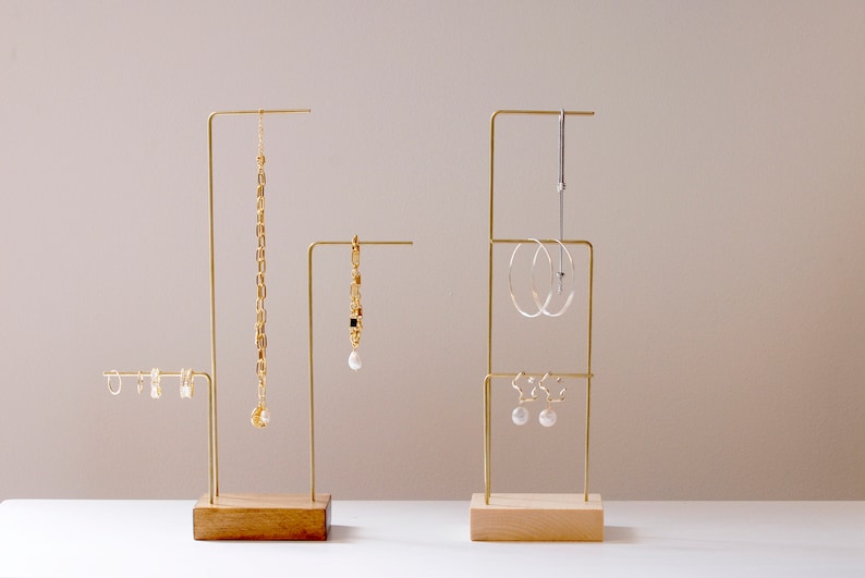 May include: Three gold metal jewelry stands with wooden bases. The stands are displaying various gold and silver earrings and necklaces.