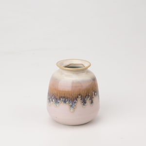 Op de afbeelding: Een kleine, ronde keramische vaas met een roze, witte en bruine glazuur. De glazuur heeft een druppel-effect, waardoor een unieke en artistieke uitstraling ontstaat.