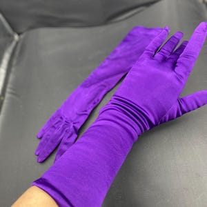 Peut inclure: Une paire de longs gants en satin violet vif. Un gant est porté, montrant la main, tandis que l'autre est à plat. Les gants sont de couleur unie, avec une texture lisse et brillante. Les gants sont probablement pour une tenue de soirée ou un costume.