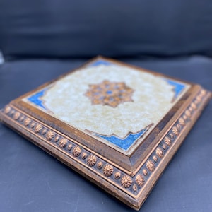 Può includere: Vassoio decorativo quadrato in legno con un centro color crema con un motivo floreale nei toni dell'arancione e del blu. Il vassoio ha un bordo blu e un bordo decorativo color rame.
