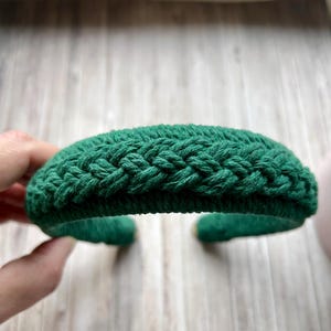 Può includere: Un cerchietto verde intrecciato in corda spessa. Il cerchietto è curvo e ha un design semplice.