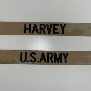 May include: Two tan fabric patches with black embroidered text. The top patch reads "HARVEY" and the bottom patch reads "U.S. ARMY".