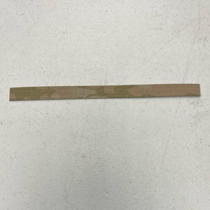May include: A thin strip of fabric with a camouflage pattern in shades of brown and green.