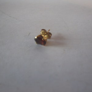 May include: A single gold earring with a small, dark red gemstone.