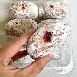 May include: A clear plastic container holding several powdered sugar-covered donuts. Each donut has a visible red jelly filling. The donuts are light brown with a generous coating of white powdered sugar, creating a sweet treat.
