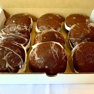 May include: A box of nine chocolate-covered marshmallow treats, individually wrapped in clear plastic. The treats are arranged in three rows of three, with the tops of the treats facing the viewer.