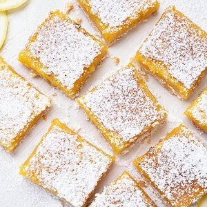 Peut inclure: Gros plan sur neuf barres au citron, chacune saupoudr&eacute;e de sucre glace, dispos&eacute;es sur une surface blanche. Les barres sont carr&eacute;es et de couleur jaune clair.