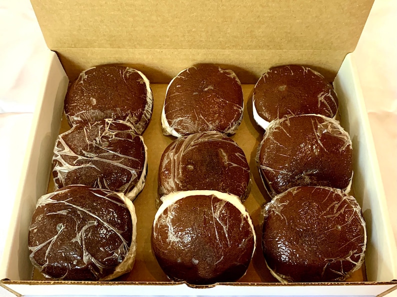 May include: A box of nine chocolate-covered marshmallow treats. The treats are individually wrapped in clear plastic and have a dark brown chocolate coating.