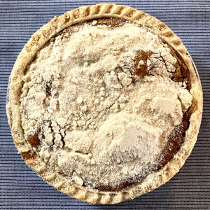 May include: A close-up of a homemade pie with a golden brown crust and a thick layer of crumb topping. The pie is on a blue and white checkered tablecloth.