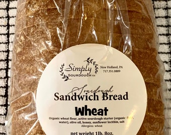 May include: A loaf of Simply Sourdough Co. wheat sandwich bread, packaged in a clear plastic bag. The label reads "Sourdough Sandwich Bread Wheat" and lists the ingredients and net weight of 1 lb. 8 oz.