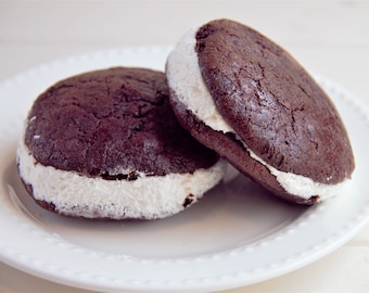 May include: Two chocolate sandwich cookies with white frosting filling on a white plate.