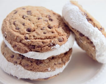 May include: Two chocolate chip cookies with white frosting between them. The cookies are stacked on top of each other. There is a third cookie with frosting on the side.