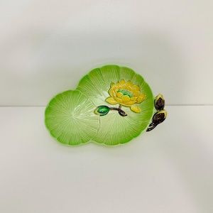 Puede incluir: Un plato de cerámica verde con forma de nenúfar con una flor amarilla y hojas verdes. El plato es perfecto para servir aperitivos o pequeñas golosinas.