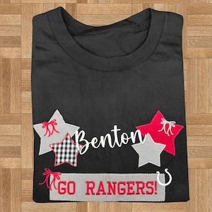 May include: A black t-shirt featuring the name Benton in white script, surrounded by gray, red, and black-and-white checkered star appliques with red bows. Below, a gray rectangular patch displays the red text GO RANGERS! with a white horseshoe.