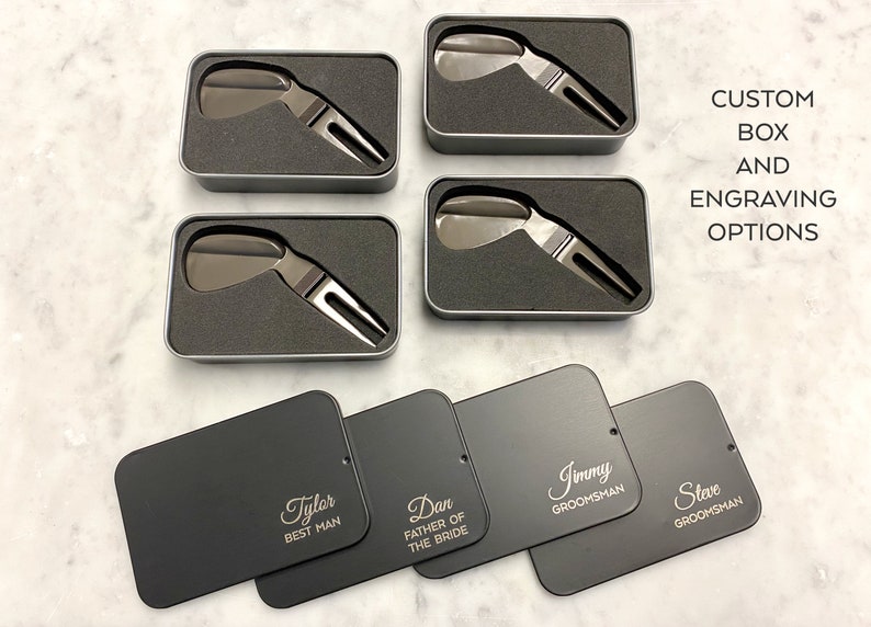 May include: Four black metal boxes with engraved names, including "Tyler Best Man", "Dan Father of the Bride", "Jimmy Groomman", and "Steve Groomman". Each box contains a silver golf divot tool. The boxes are arranged in two rows of two. The text "CUSTOM BOX AND ENGRAVING OPTIONS" is written in white on a gray background.