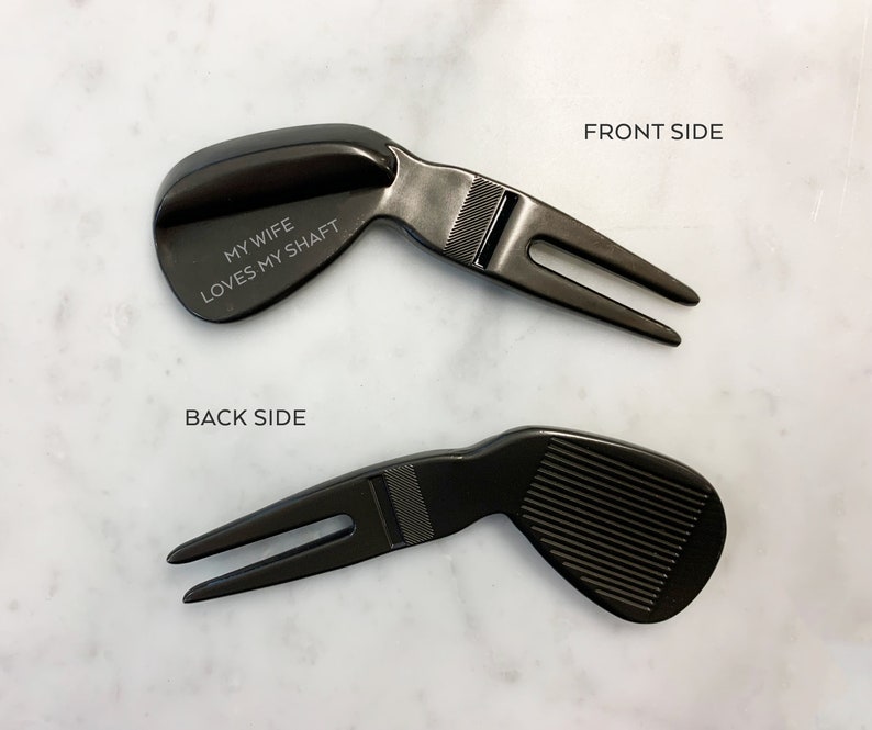May include: Black golf ball divot tool with a golf club head design. The back side of the tool has the text "My wife loves my shaft".