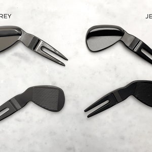 May include: Two sets of golf divot tools, one in matte grey and one in jet black. Each tool has a golf club head shape and a two-pronged fork.