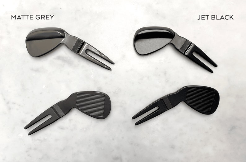 May include: Two sets of golf divot tools, one in matte grey and one in jet black. Each tool has a golf club head shape and a two-pronged fork.