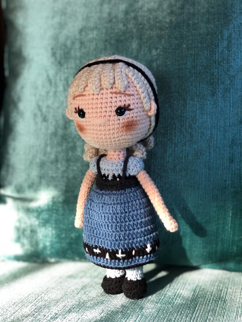 K&ouml;nnte beinhalten: Eine geh&auml;kelte Puppe mit blonden Haaren, einem blauen Kleid mit schwarzem und wei&szlig;em Besatz und schwarzen Schuhen.