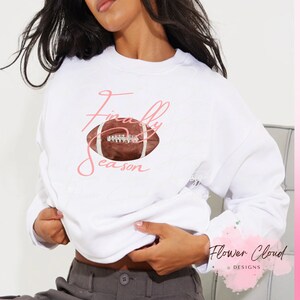 May include: White sweatshirt with a pink graphic that says "Finally Season" and a brown football.