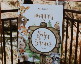 May include: A white sign with a wooden background and a circle that says "Baby Shower" with the date 5.5.24. The sign is decorated with woodland animals, including a deer, bear, fox, hedgehog, squirrel, owl, and raccoon. The sign says "Welcome to Maggie's Baby Shower 5.5.24".