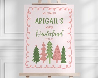 以下が含まれることがあります： イーゼルに立てられたウェルカムサイン。テキスト「Welcome to Abigail's Winter Onederland 12.17.25」が書かれています。ピンク色の縁取りがあり、緑とピンクのクリスマスツリーが描かれています。