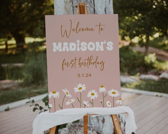 May include: A pink welcome sign with white daisies at the bottom. The sign says "Welcome to MADISON'S first birthday 3.1.24".