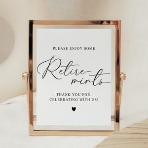 May include: A framed sign with gold trim and a white background. The sign reads "Please enjoy some Retire-mints. Thank you for celebrating with us!" in black script. A small black heart is at the bottom.