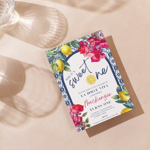Peut inclure: Une carte d'invitation blanche avec une bordure de carreaux bleus et blancs et un motif floral. Le texte sur la carte indique "She's a sweet one" et "Please join us to celebrate La Dolce Vita". L'invitation est pour le premier anniversaire de Mackenzie.