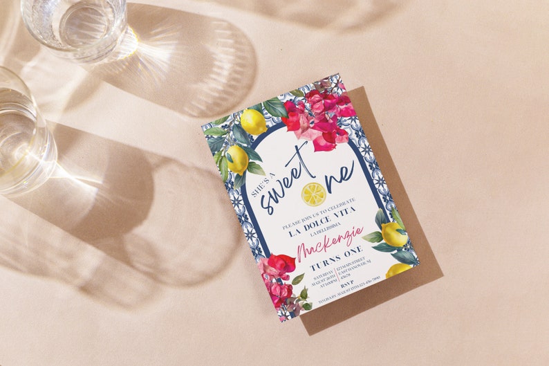 Peut inclure: Une carte d'invitation blanche avec une bordure de carreaux bleus et blancs et un motif floral. Le texte sur la carte indique "She's a sweet one" et "Please join us to celebrate La Dolce Vita". L'invitation est pour le premier anniversaire de Mackenzie.