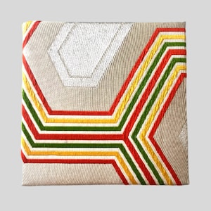 May include: A beige fabric clutch with a geometric pattern of red, yellow, and green stripes. The pattern is embroidered on the fabric.