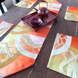 以下が含まれることがあります： 赤と金のテーブルランナー、4つのプレースマット、赤と金のデザインのティーポットが置かれたテーブルセッティング。ティーポットは、赤いトレイの上に置かれ、4つの小さな赤いボウルが置かれている。