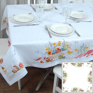 May include: White linen tablecloth with an embroidered Easter design. The design features a basket of colorful eggs, chicks, and spring flowers. The tablecloth has a scalloped edge.