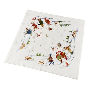 May include: White linen tablecloth with an embroidered winter scene. The design features children carrying lanterns, stars, and a crescent moon. There are also small houses and trees in the scene.