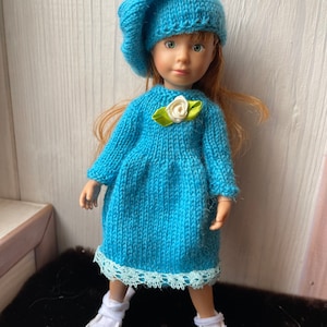 May include: A blue knitted dress with a white flower accent and a matching blue knitted beret. The doll is wearing white sneakers.
