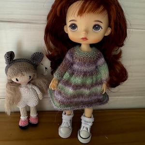 May include: Two handmade dolls. One doll has red hair and wears a striped purple and green dress with white sneakers. The other doll is smaller, crocheted, and wears a gray hat and white dress with pink shoes.