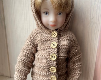 May include: A brown knitted hooded sweater with a button closure and matching brown pants. The doll is wearing the sweater and pants.