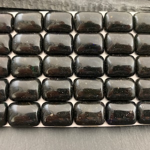 Puede incluir: Una colección de treinta y dos baldosas de vidrio negro brillante y rectangular dispuestas en una cuadrícula. Cada baldosa tiene esquinas redondeadas y una superficie reflectante, con sutiles motas de color visibles. Las baldosas están sobre una superficie blanca.