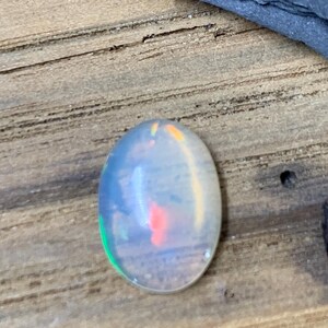 May include: Oval-shaped opal gemstone with a milky white base and flashes of green, orange, and red.